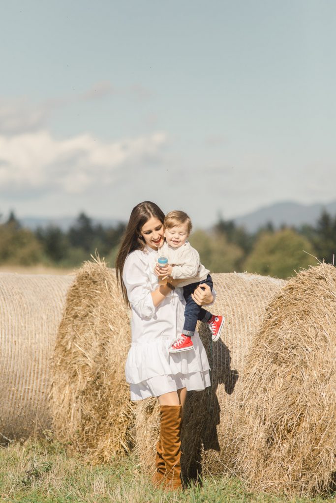 mladá mama v bielych šatách nesie syna na rukách počas fotenia